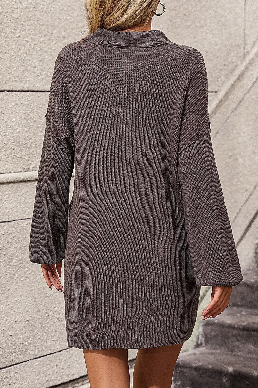 Person wearing a brown textured dress against a stone wall.
