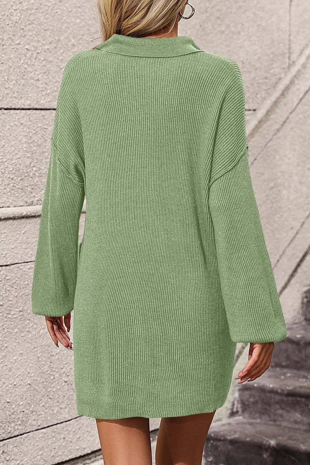 Green ribbed dress worn by a person against a textured wall.