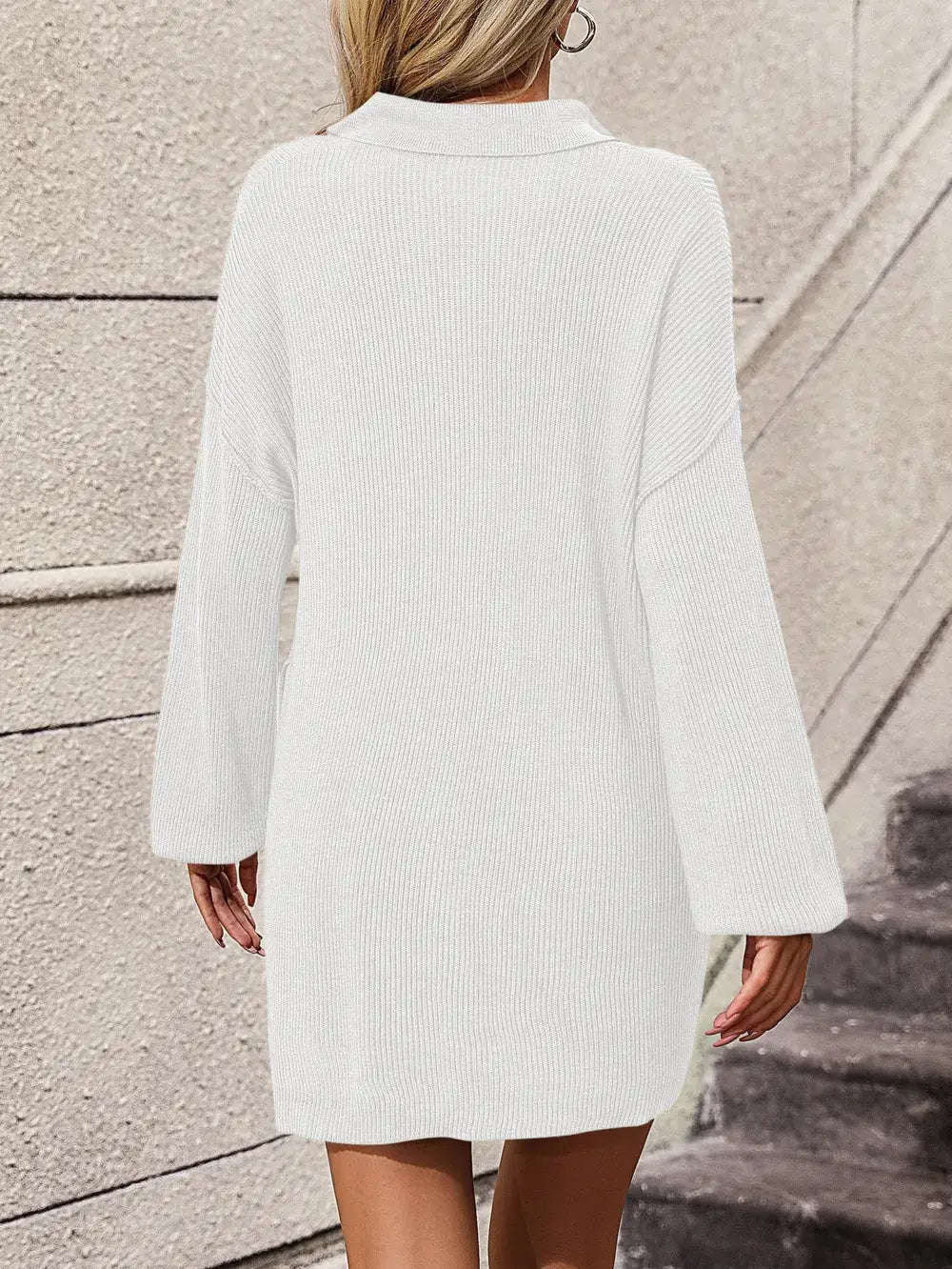 Person wearing a light gray ribbed sweater dress standing against a neutral wall.