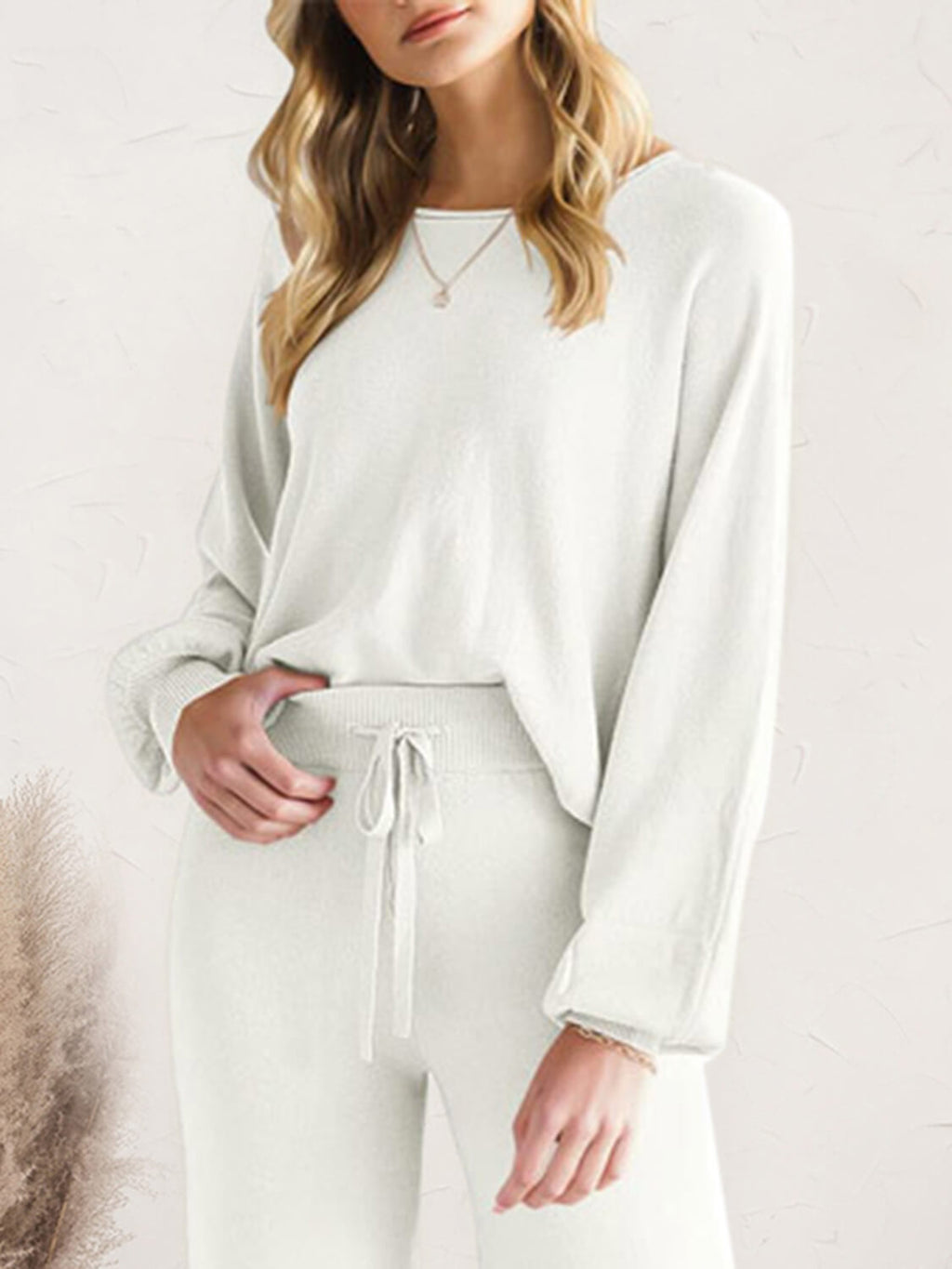 Person wearing a white long-sleeve top and pants on a light background